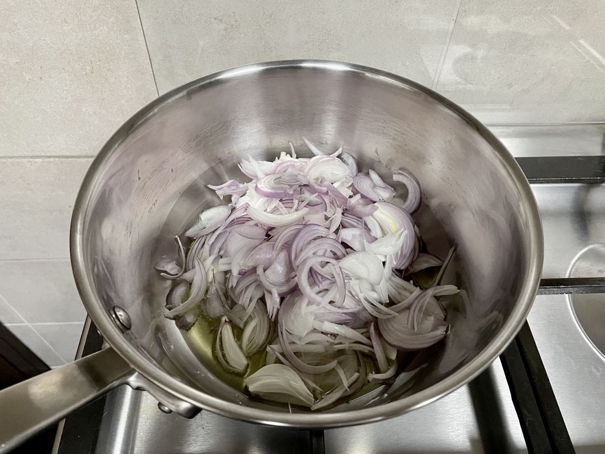 A saute pan with oil and sliced red onions.