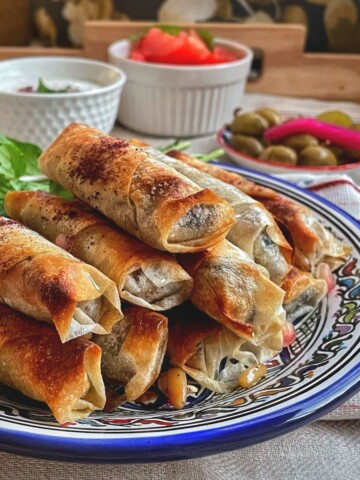 A plate with baked musakhan rolls stacked and served with salad.