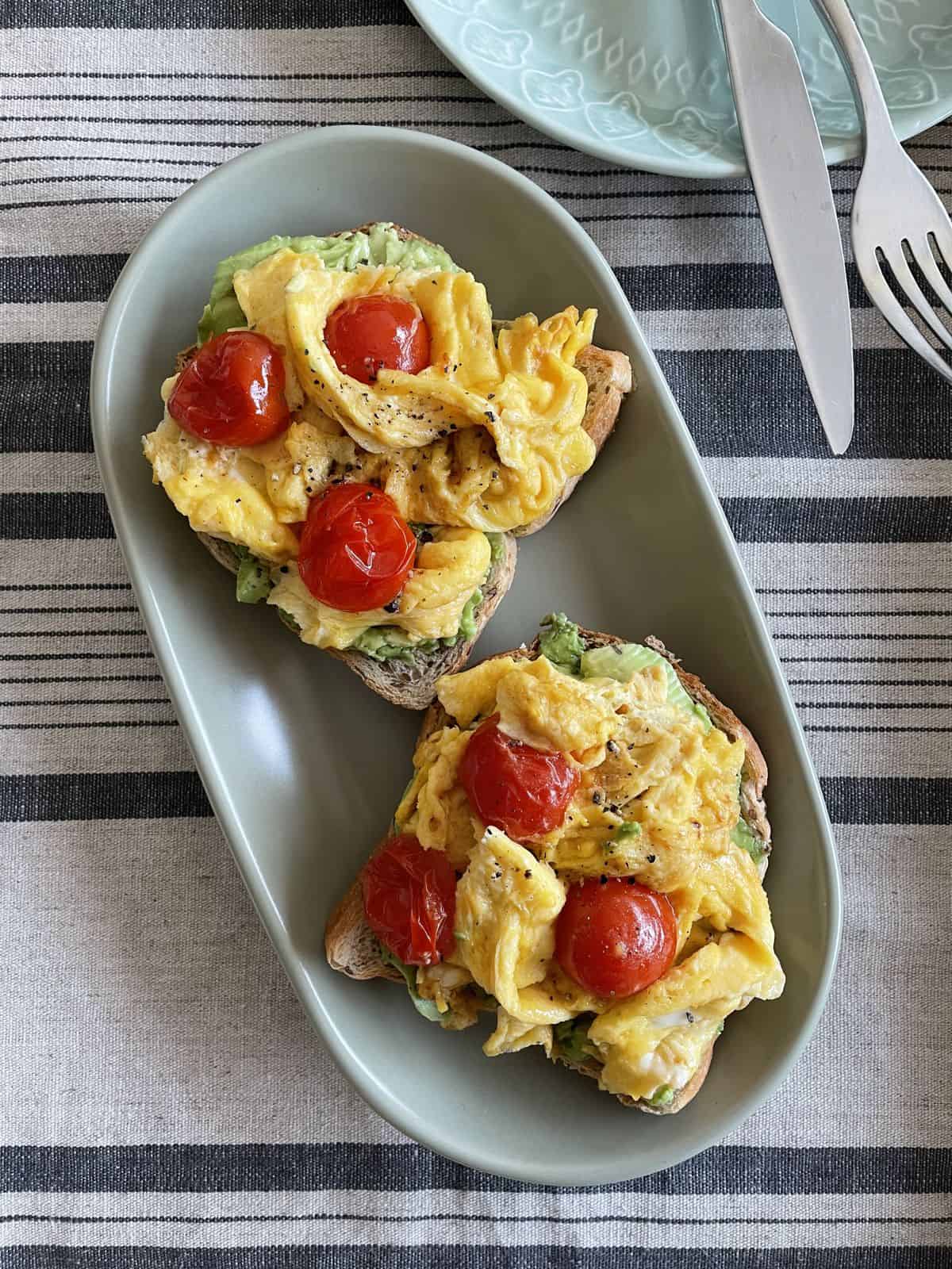 Two breakfast Avocado toast topped with scrambled eggs with tomatoes. 