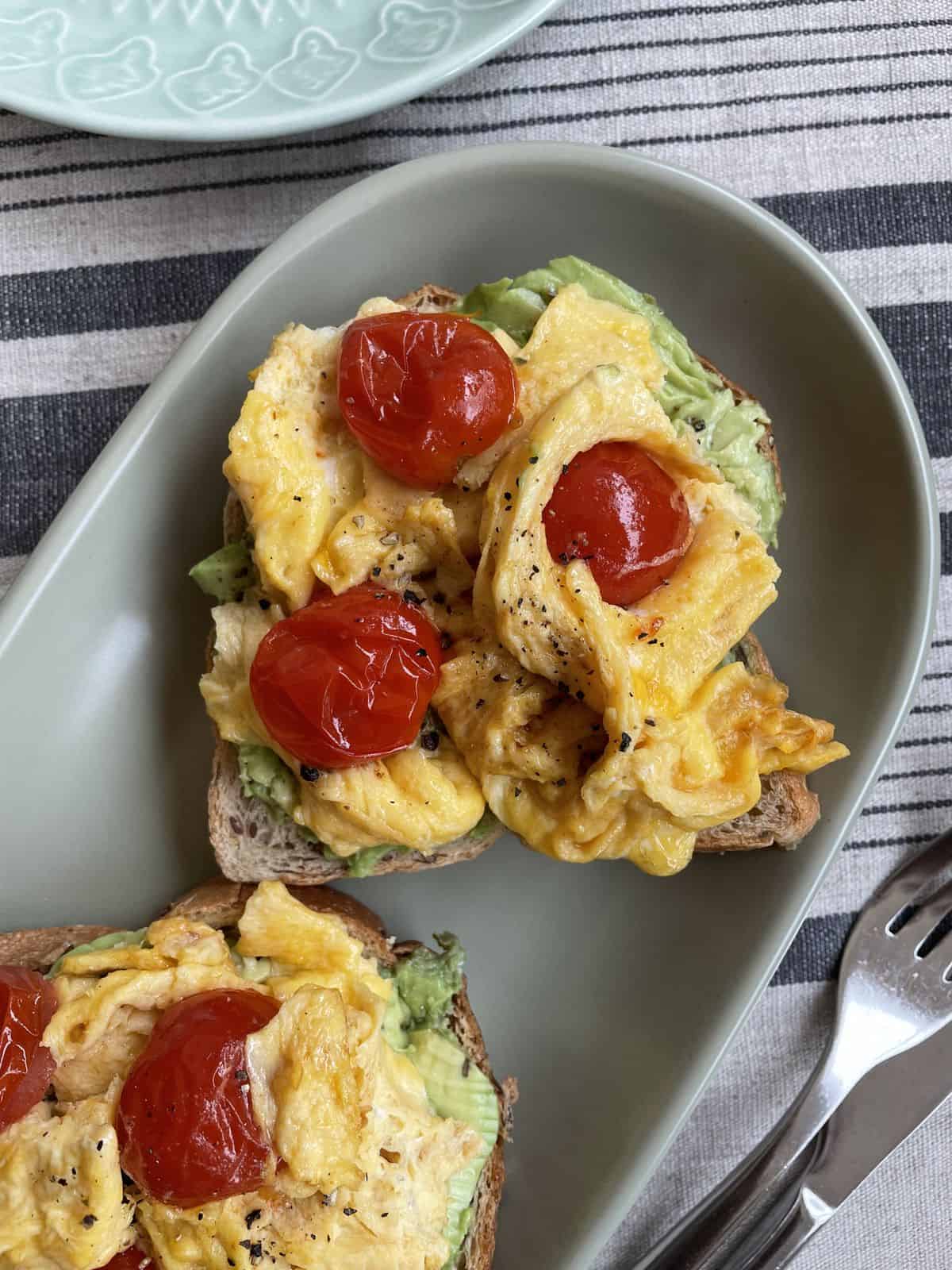 Scrambled eggs with tomatoes on a avocado toast served