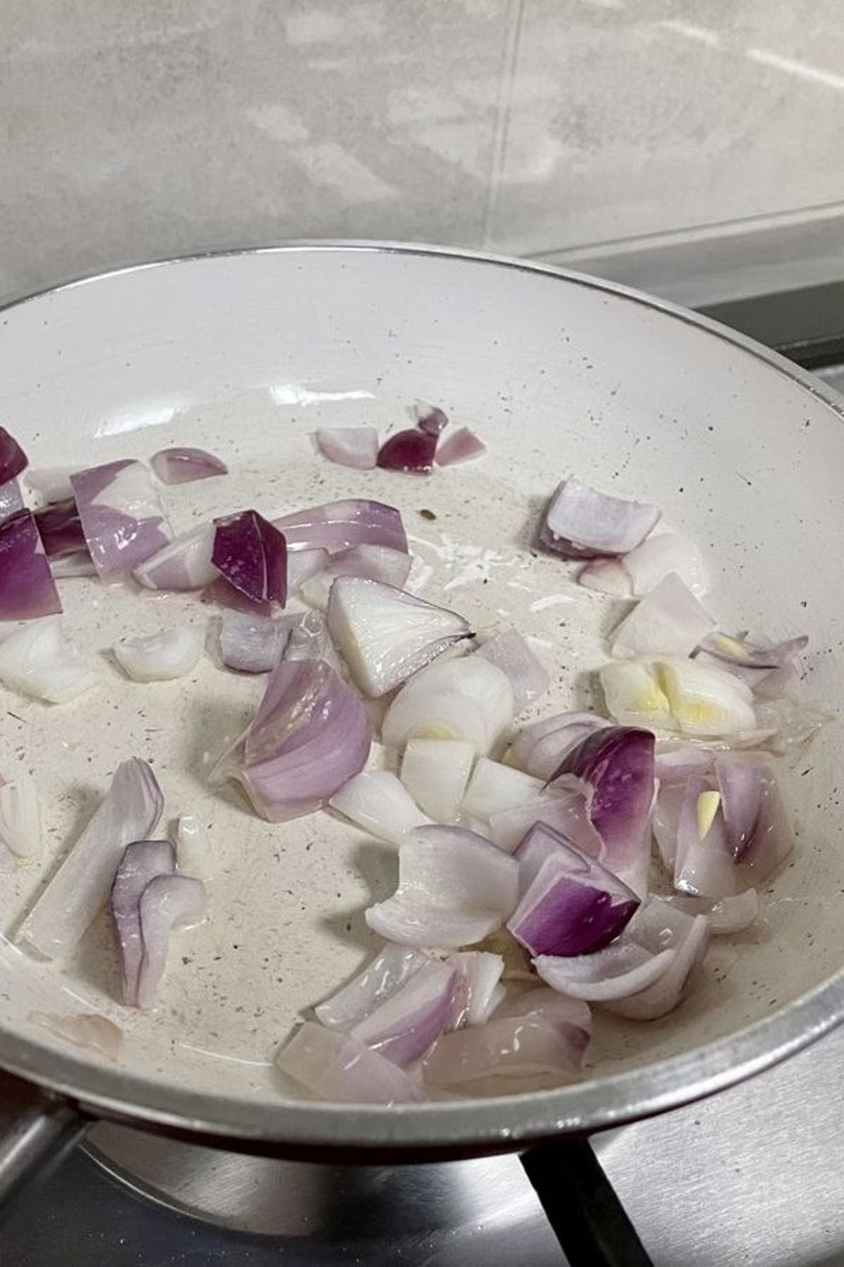 A pan on the stove with roughly chopped onions in oil.