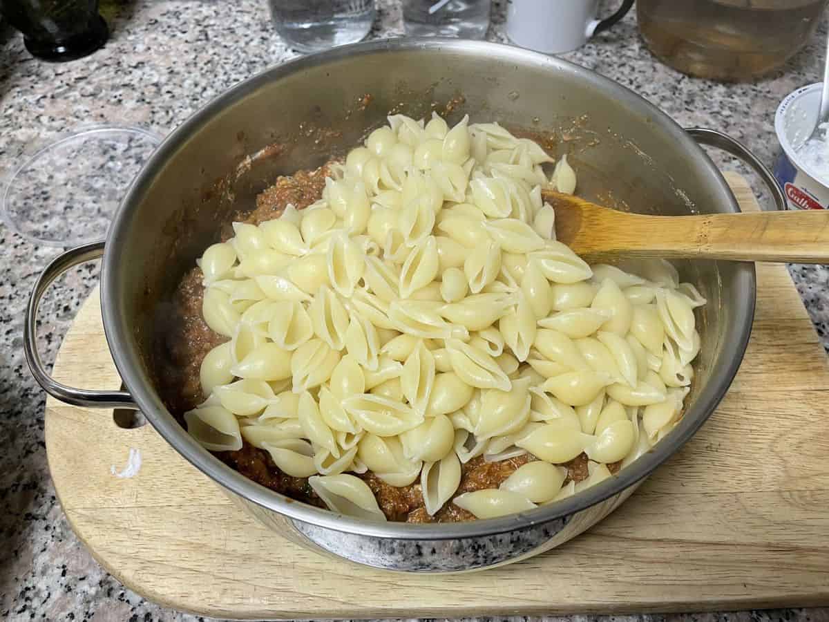 A saute pan with boiled and drained pasta over the beef sauce. 