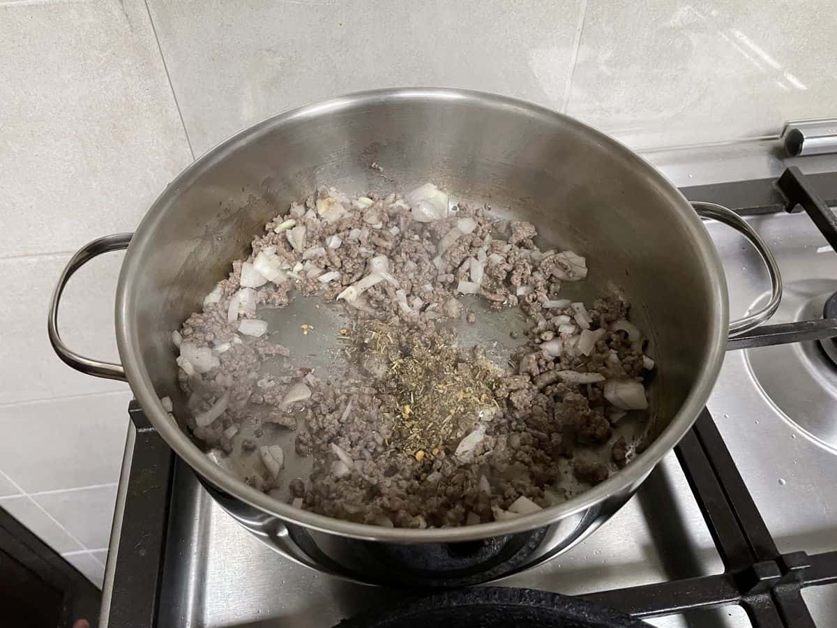 A saute pan on the stove with seasoned ground beef.