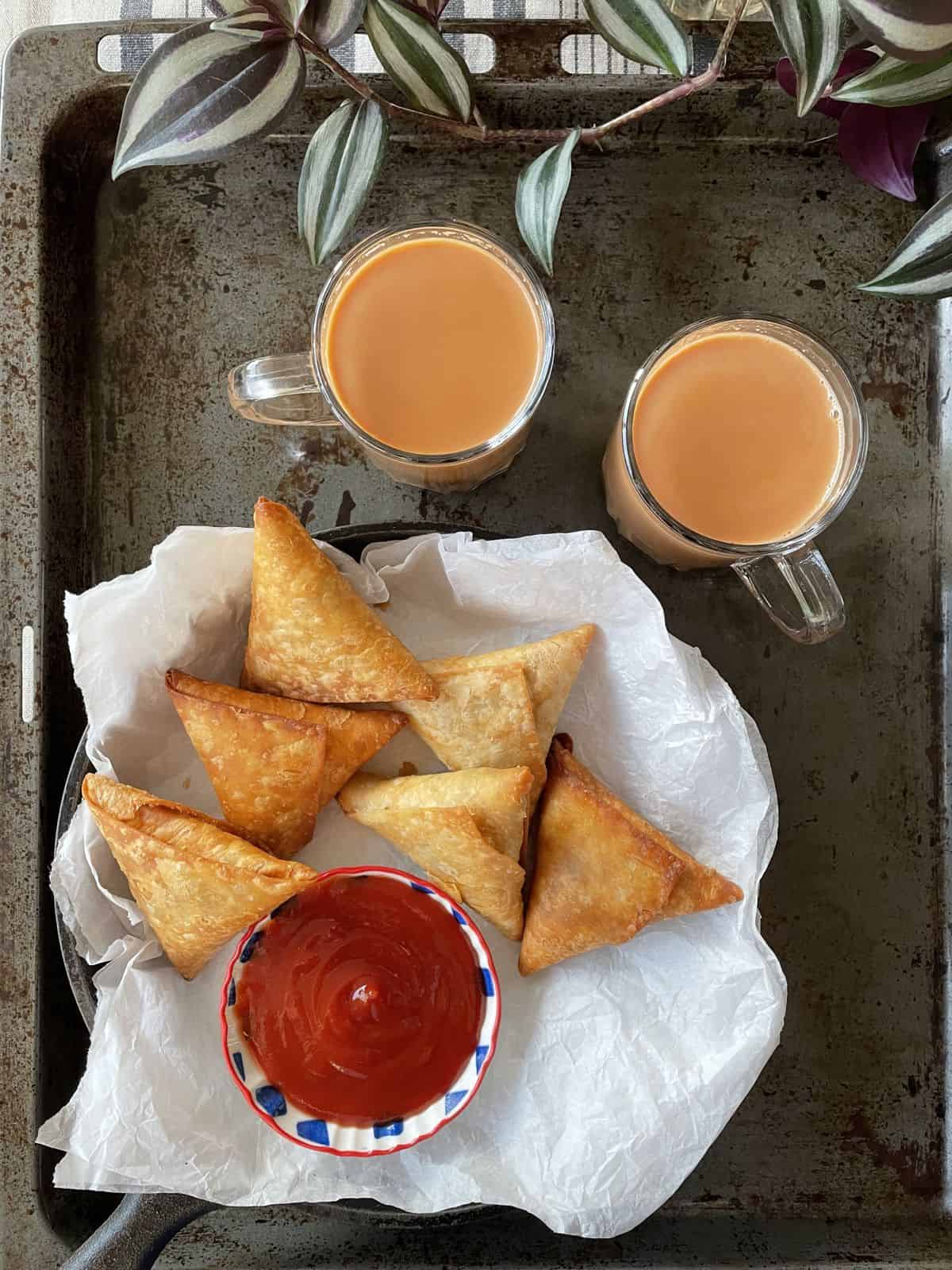 Keema samosas served with two cups of chai and ketchup.