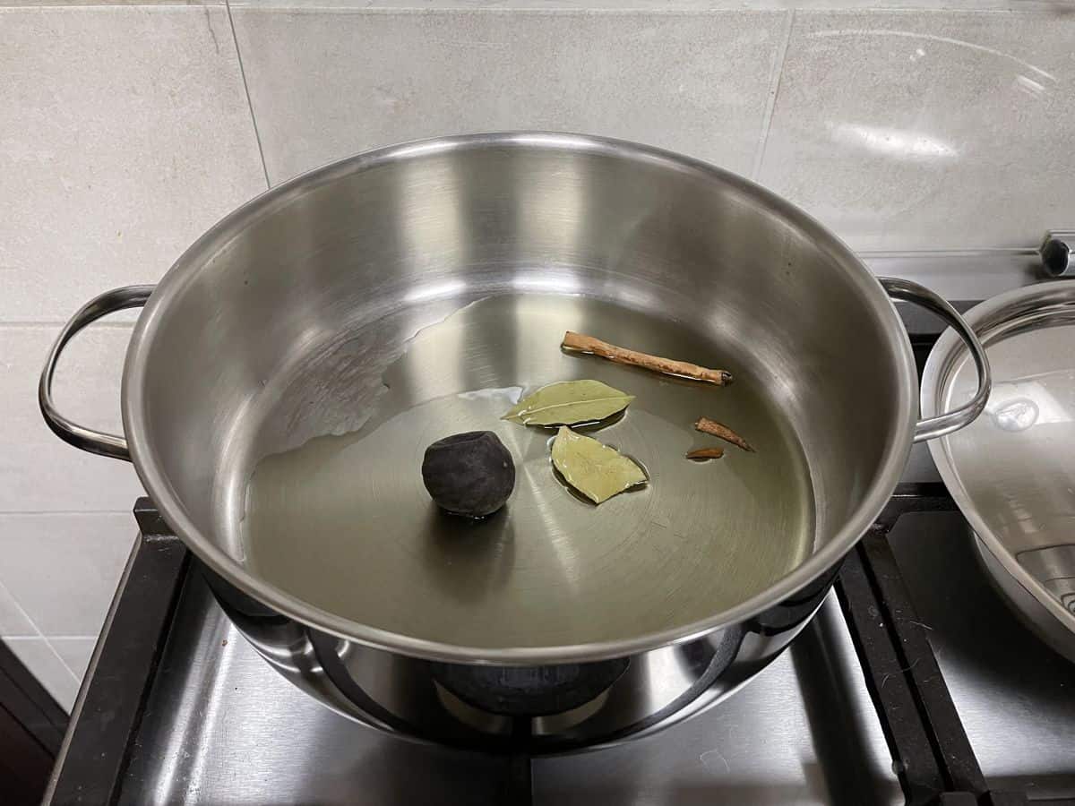 A stainless steel wide sauce pot on stove with oil and whole spices. 