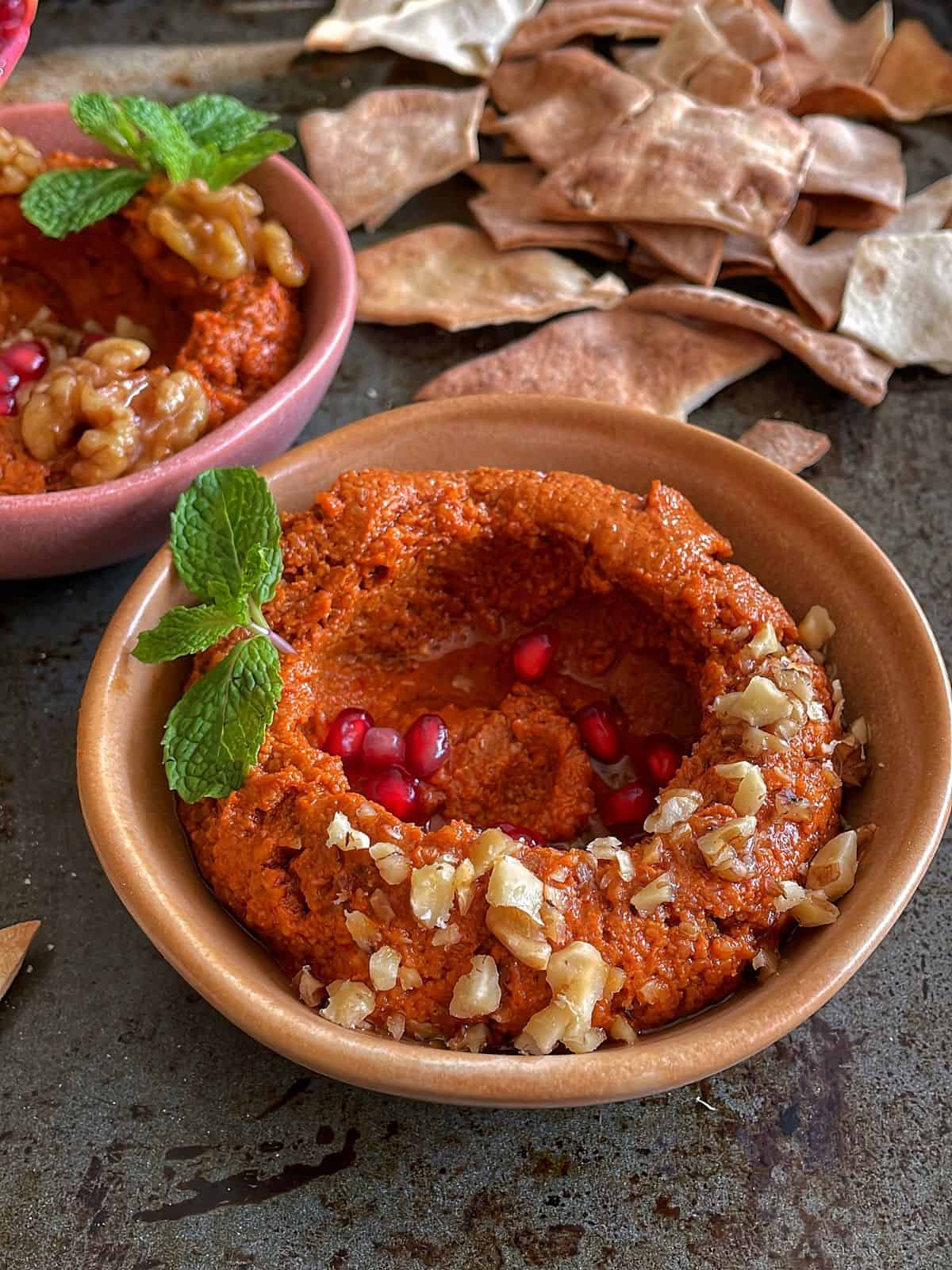 A bowl of mhammara dip garnished with walnuts and pomegranate.