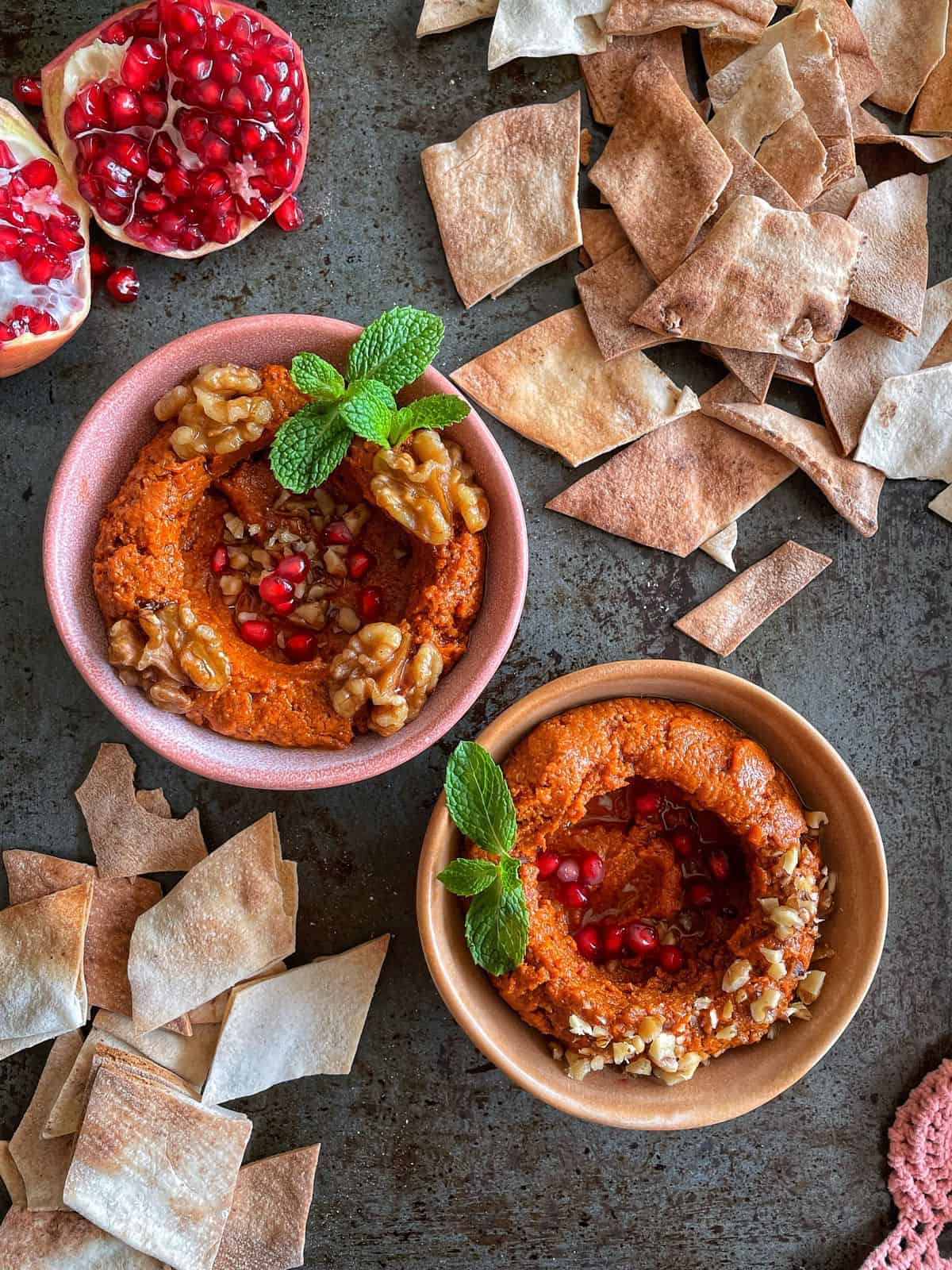 Two bowls of garnished mhammara dip served with pita chips.