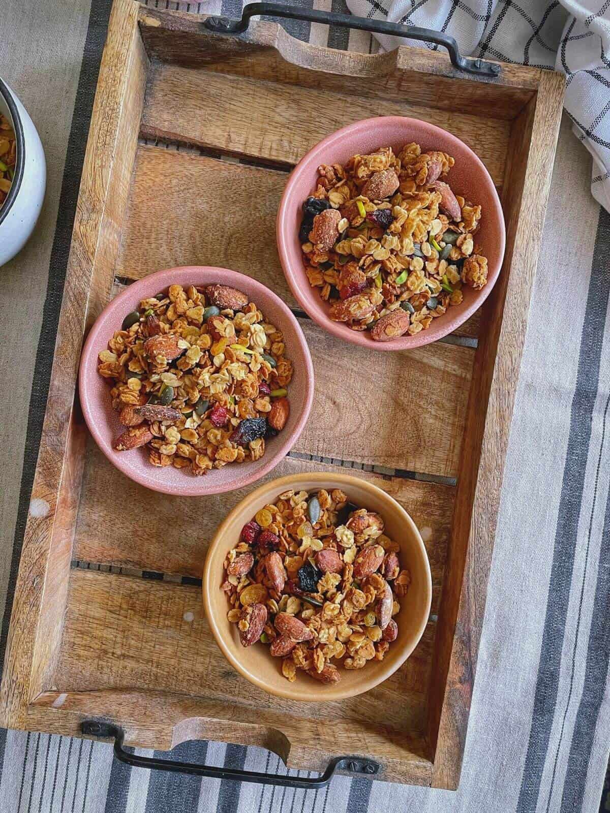 Three mini bowls of granola in a wooden serving tray.