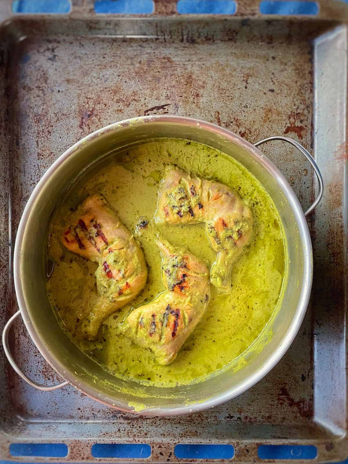 A pot of green coloured curry with chicken leg quarters