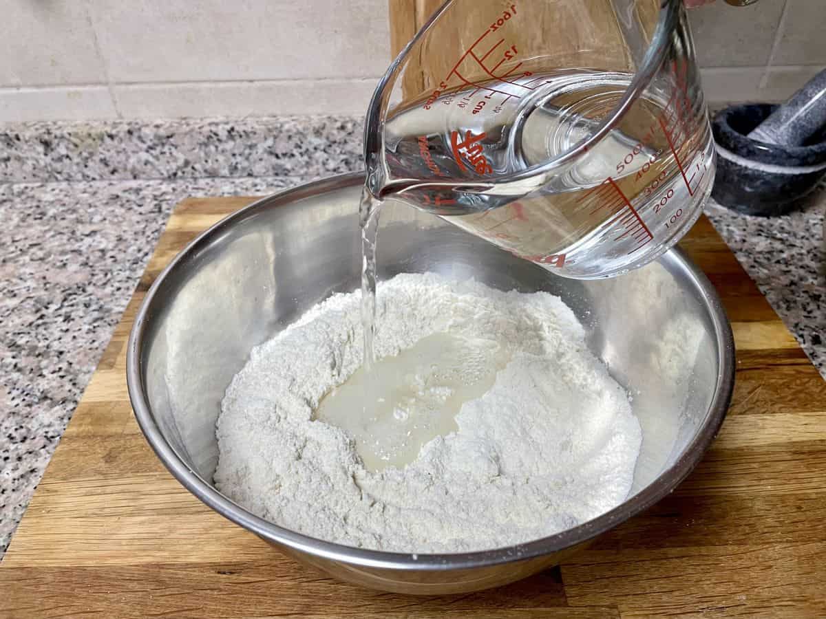 A jar of water being poured over the bowl of flour.