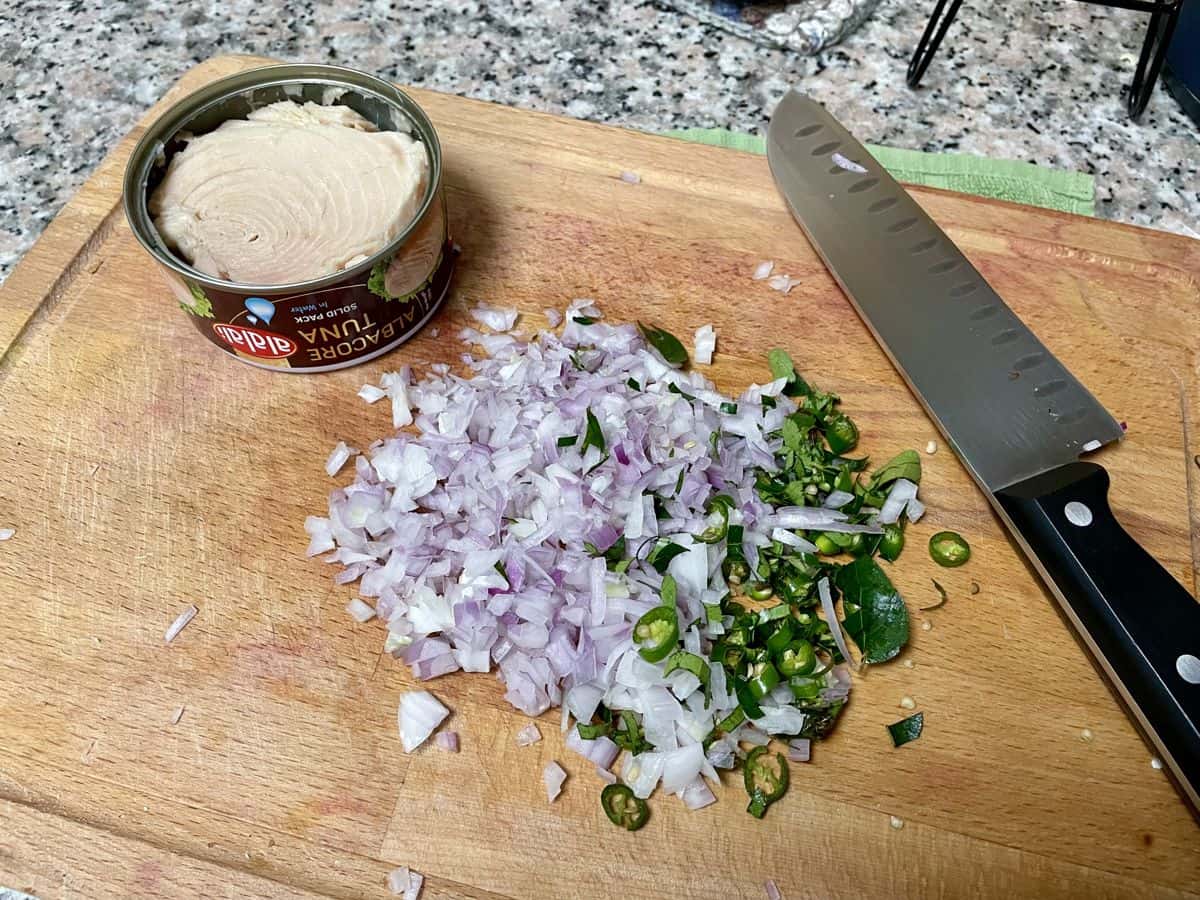 Chopped red onion and opened can of tuna on a cutting board