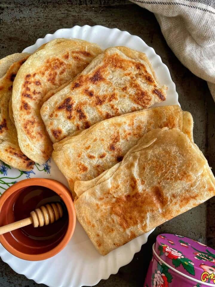 A stack of Msemen served with a bowl of honey. 