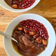 Two bowls of breakfast ragi porridge topped with ghee and almonds, pomegranate arils.