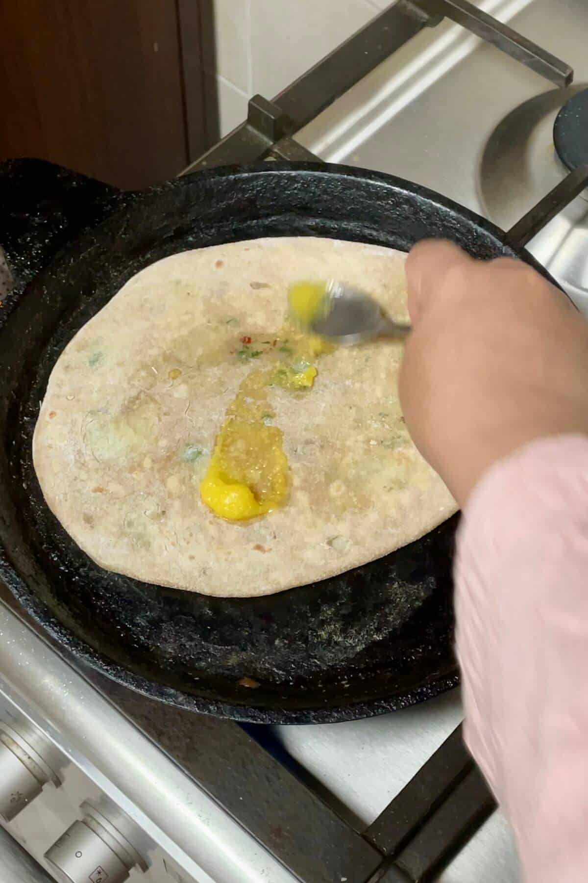 Applying ghee to aloo paratha.