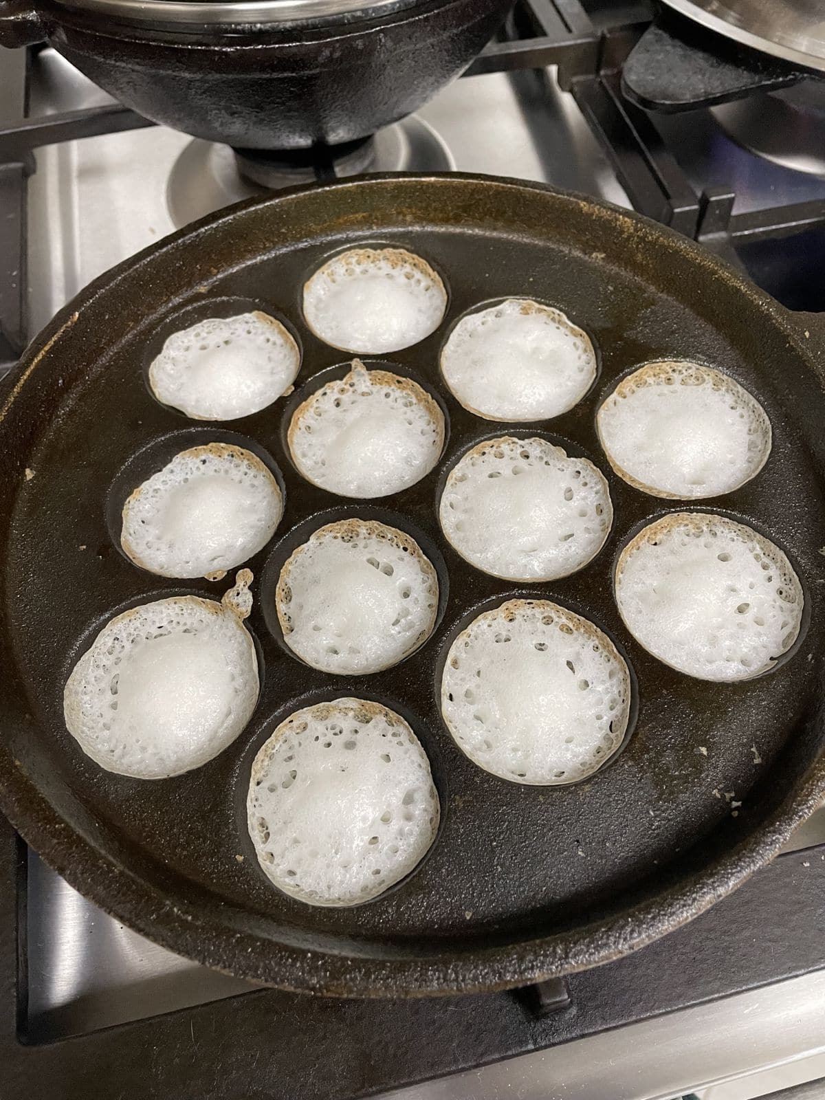 An appe pan with a dozen of mini appams on it.