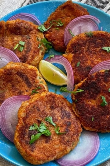 Fried shami kababs with onions and lime on a blue plate.