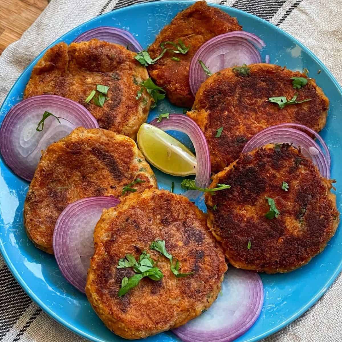 Fried shami kababs with onions and lime on a blue plate.