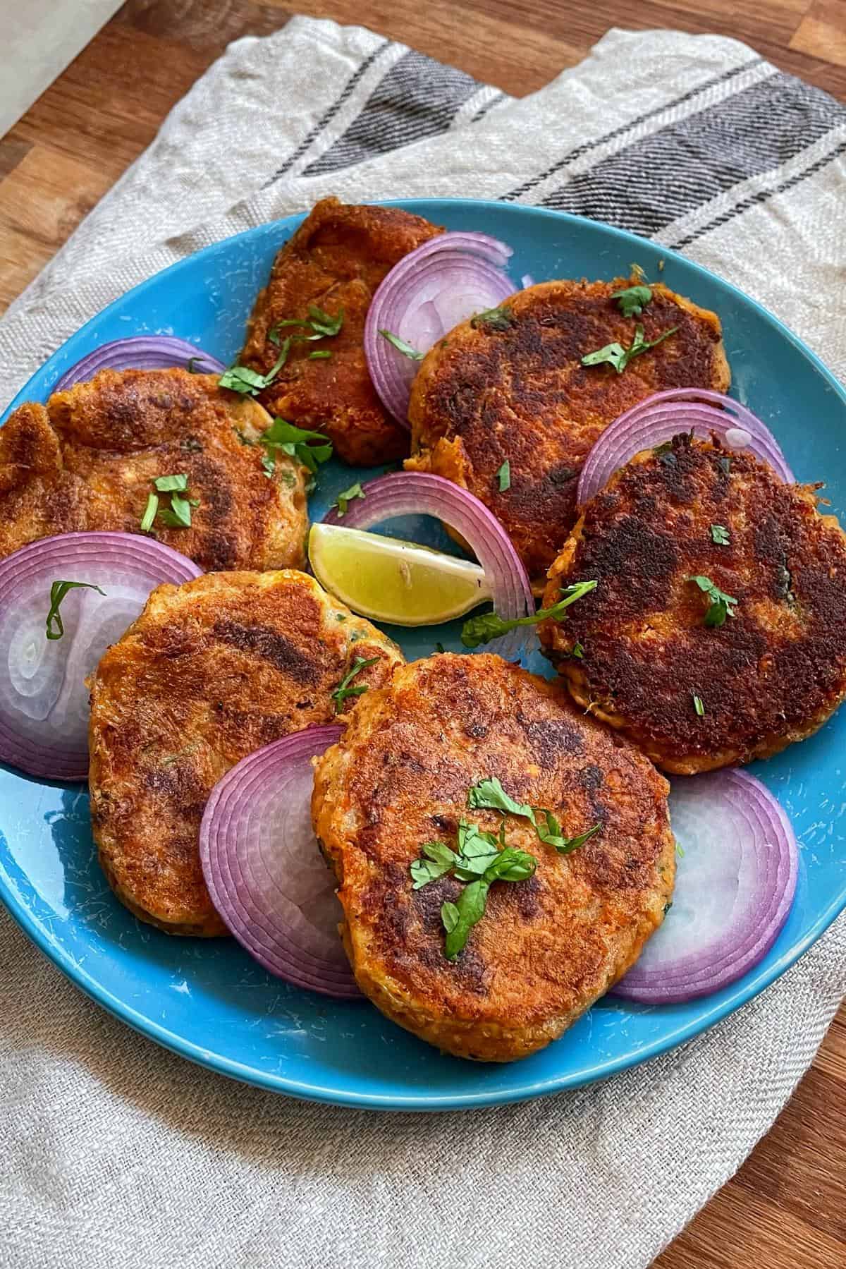 A blue plate topped with fried shami kababs and onions.