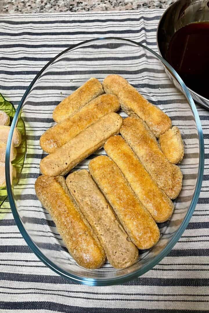 Ladyfingers dunked and assembled in an oval dish.