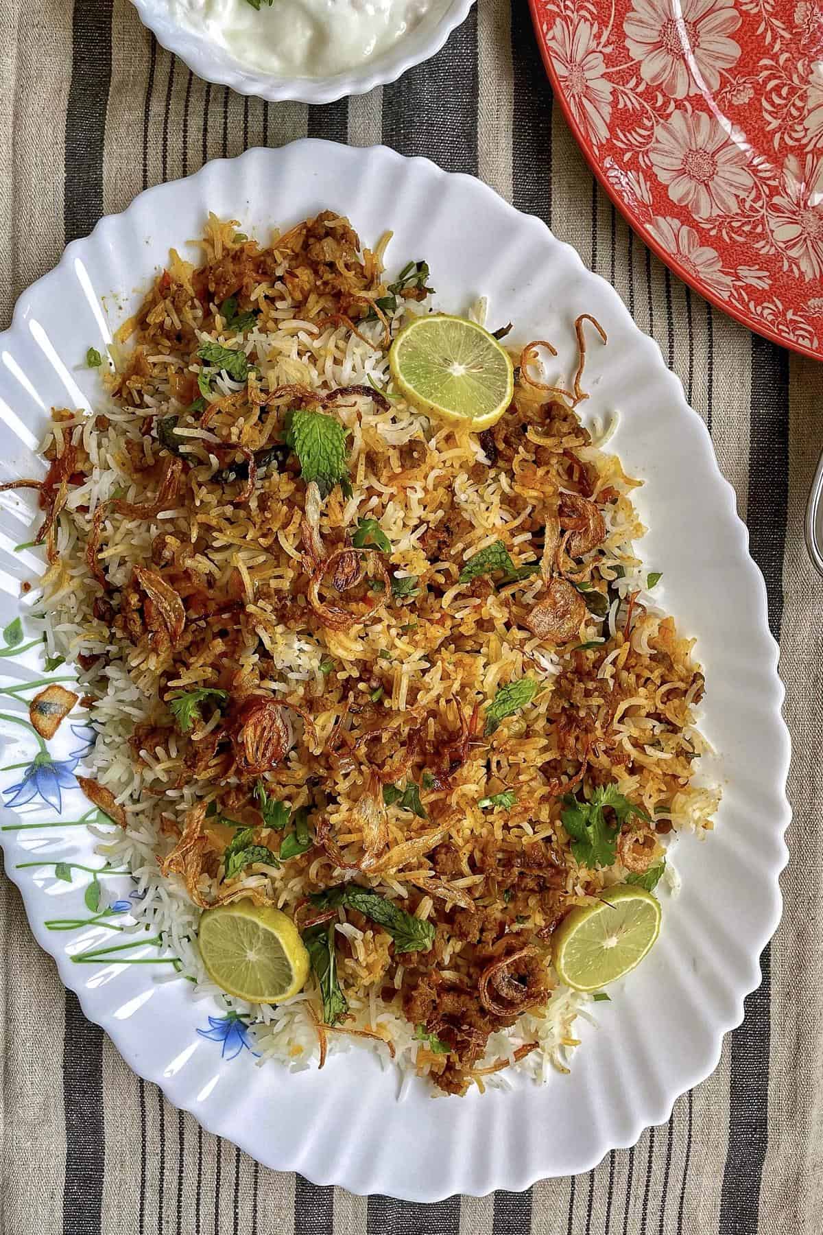 Keema Biryani rice dish served on a white platter with lemon slices and herbs.