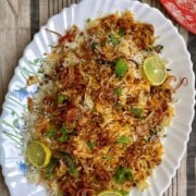 Keema biryani rice with herbs, and lime garnishes on a white decorative plate.