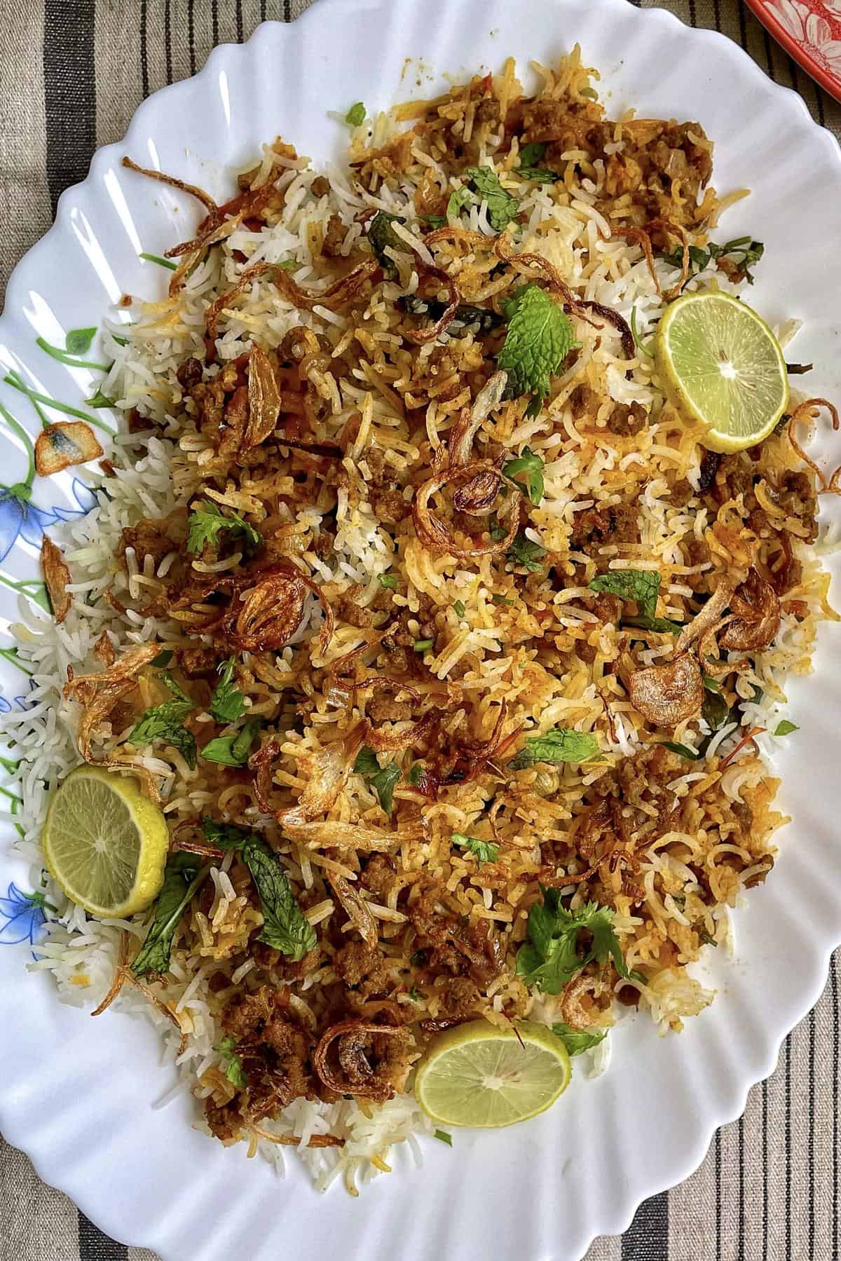 A platter of keema biryani garnished with lime slices and fried onions. 
