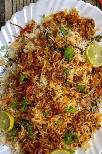Keema biryani rice with herbs, and lime garnishes on a white decorative plate.