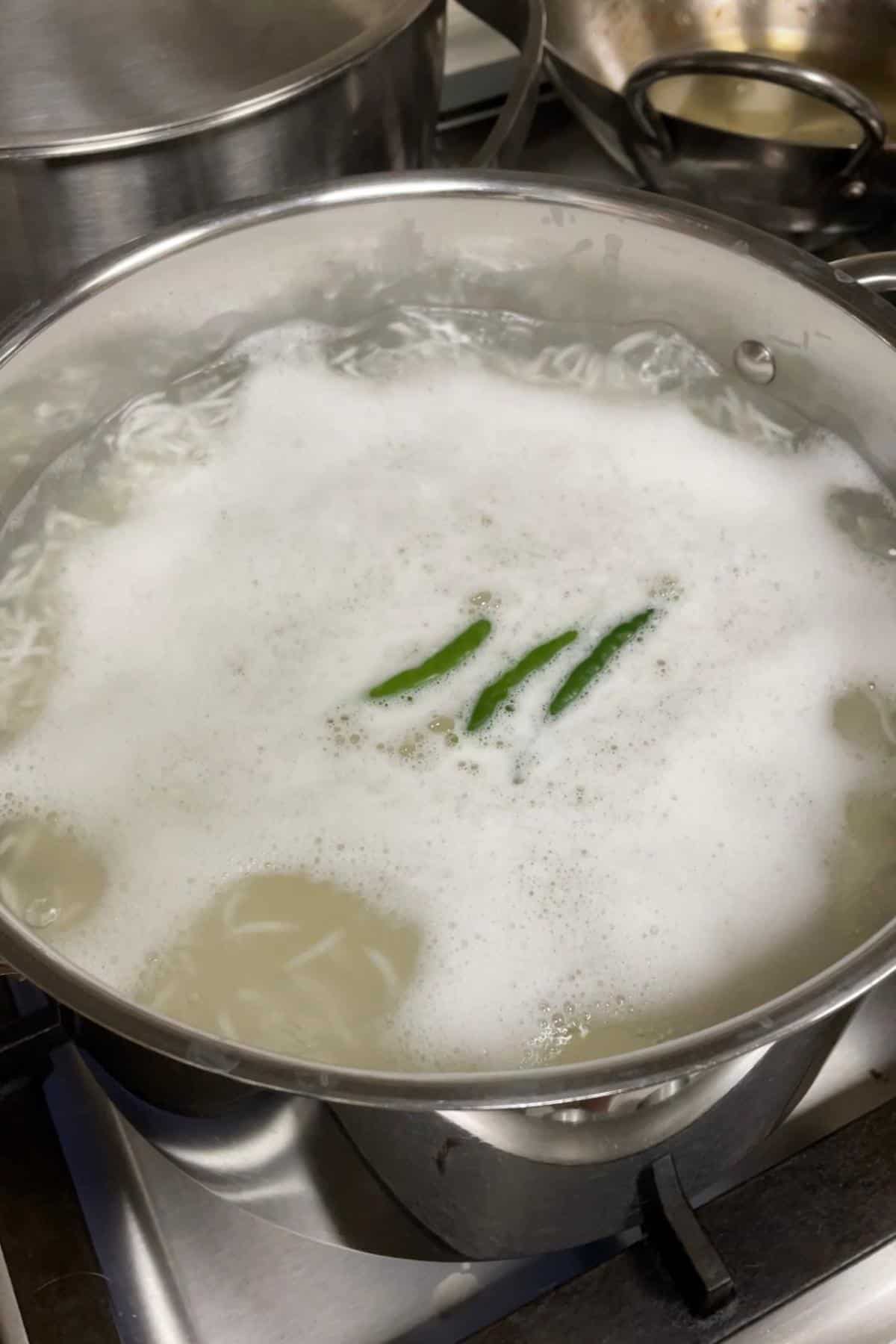 Steaming pot with boiling water and green chillies, ready for par-boiling rice.