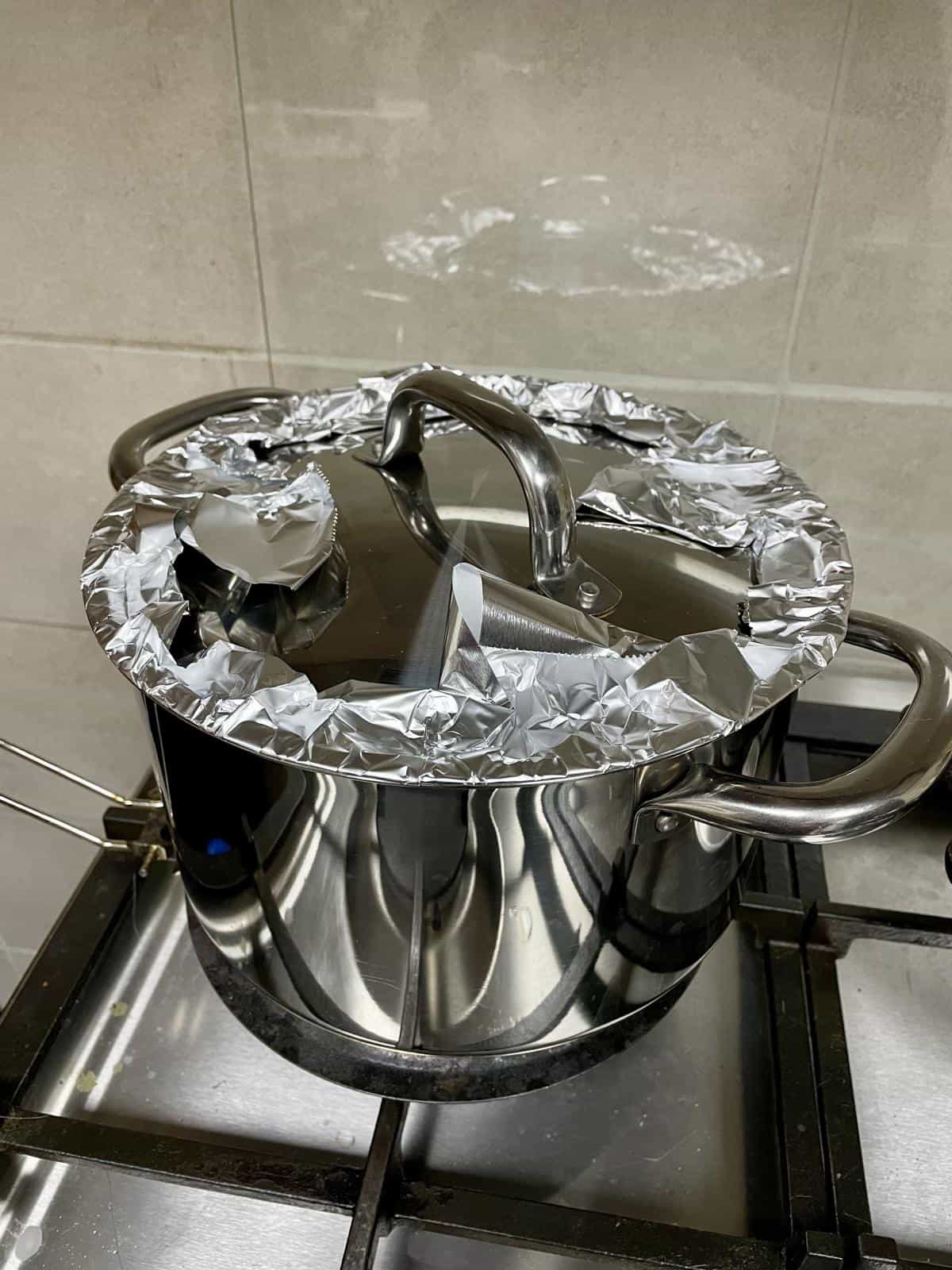 A steel pot with aluminum foil lid on stovetop for finishing off keema biryani cooking.