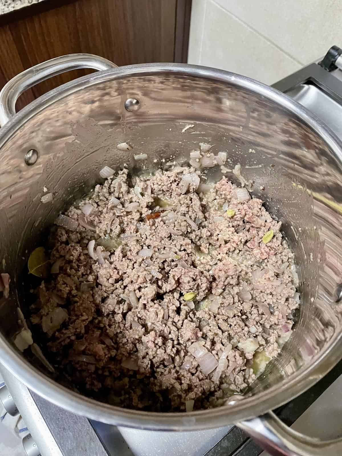 Minced cooked ground beef with onions in stainless steel pot, ready for recipe preparation.