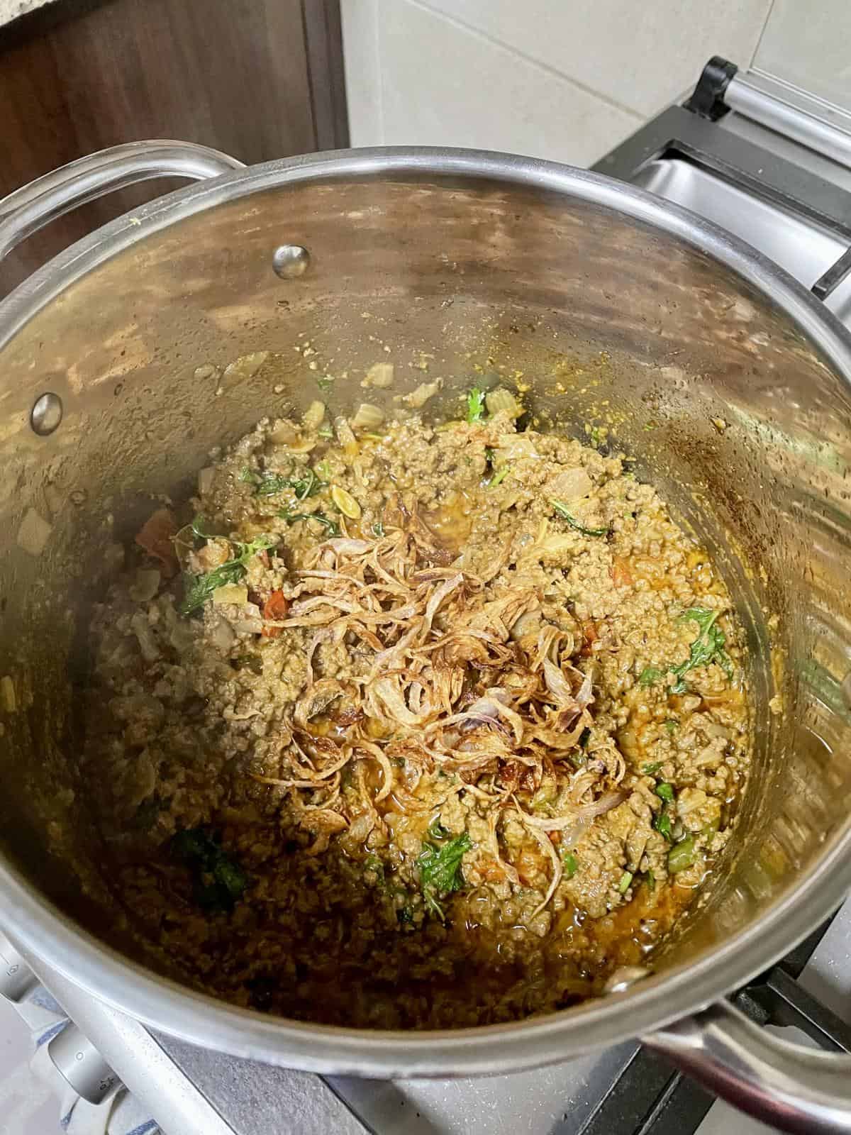Seasoned ground beef with onions and herbs in a stainless steel pot.