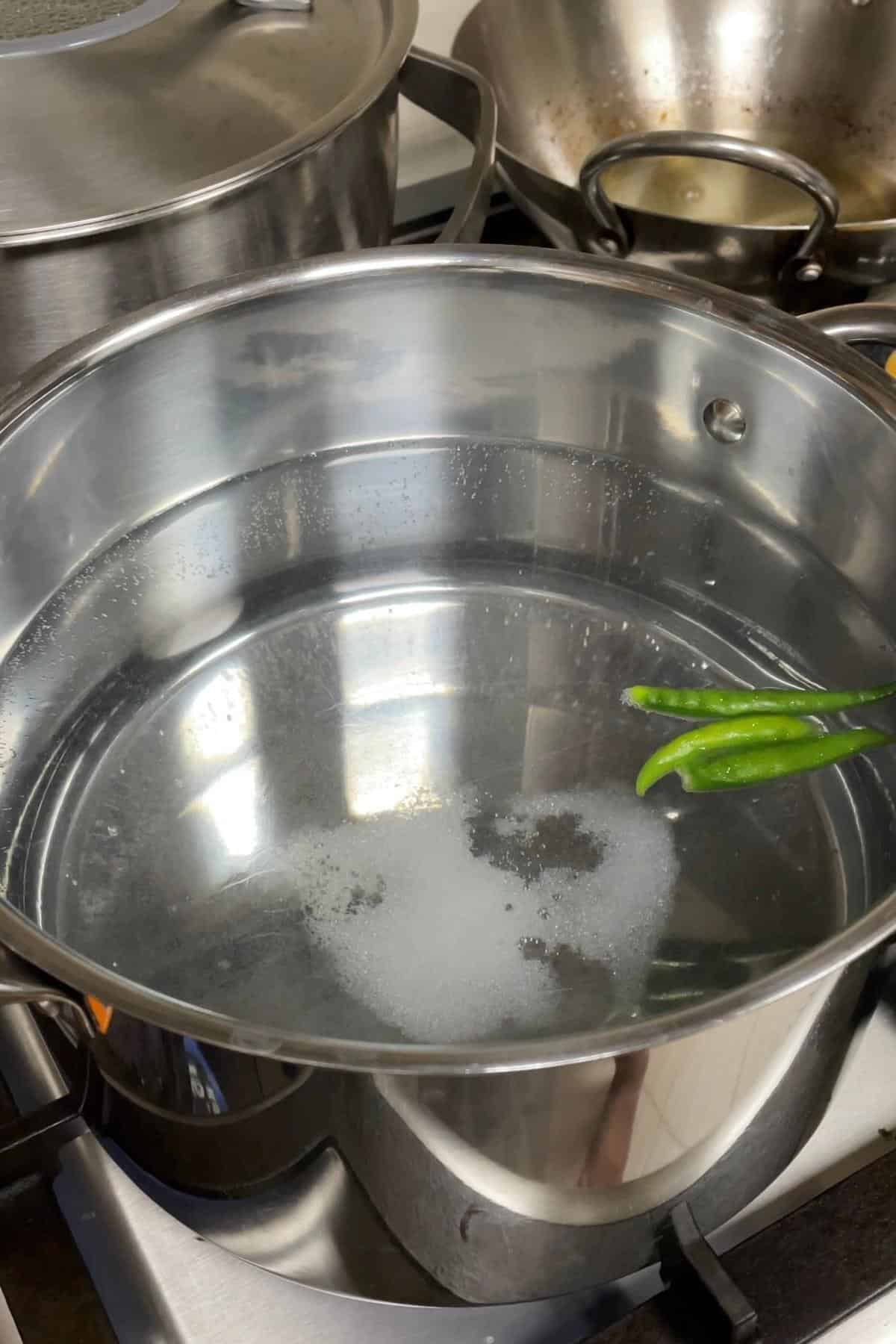Steaming water in a pot with green chili peppers, preparing for par-boiling rice cooking process.