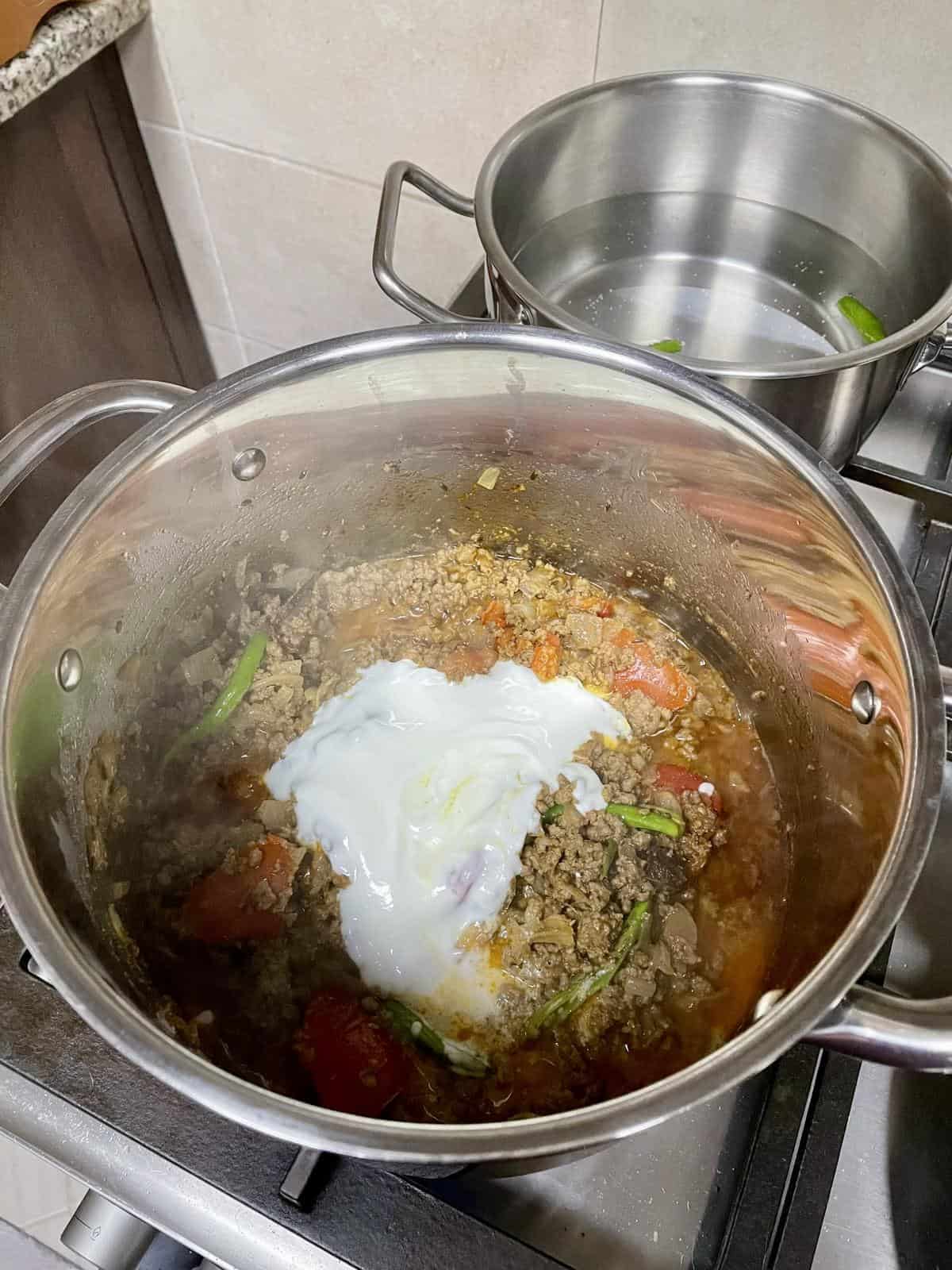 Savory ground beef stew with vegetables and a dollop of sour cream in a stainless steel pot.