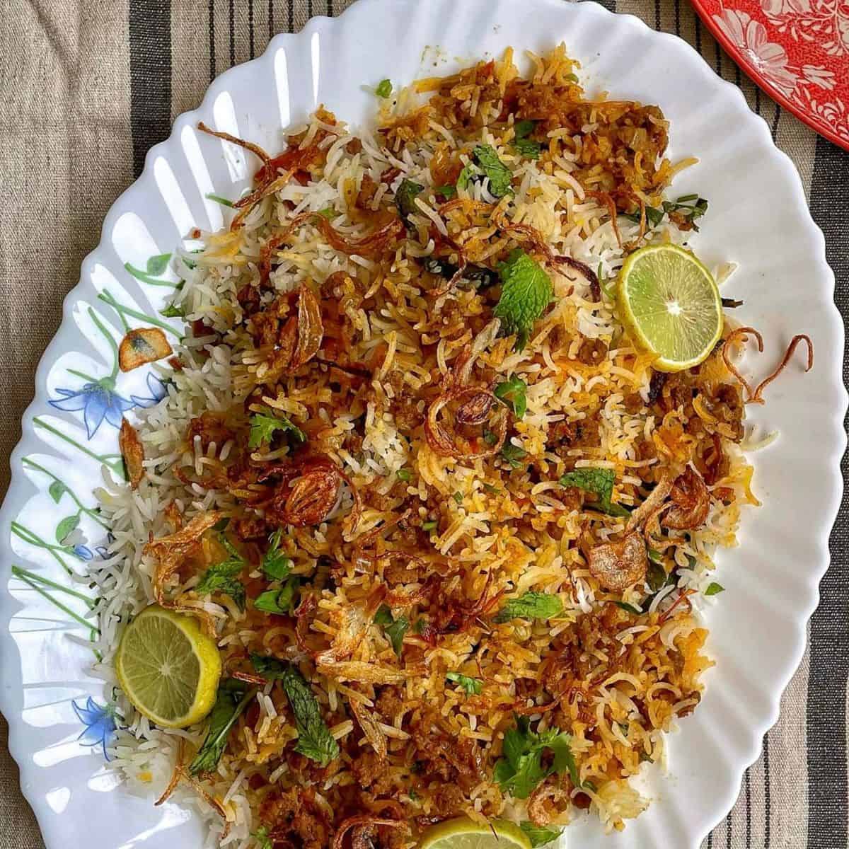 Keema biryani rice with herbs, and lime garnishes on a white decorative plate.