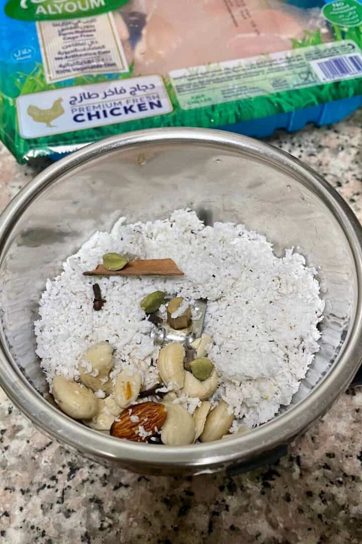 A mixie jar with grated coconut, soaked nuts and whole spices.
