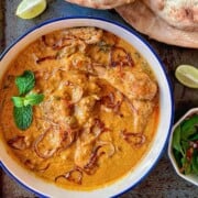 A bowl of chicken hyderabadi curry with lime wedges and naan bread.