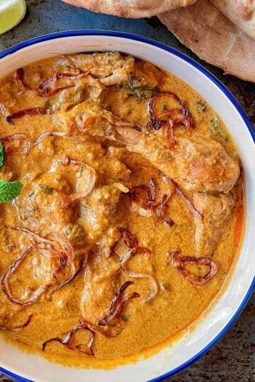 A bowl of chicken hyderabadi curry with lime wedges and naan bread.