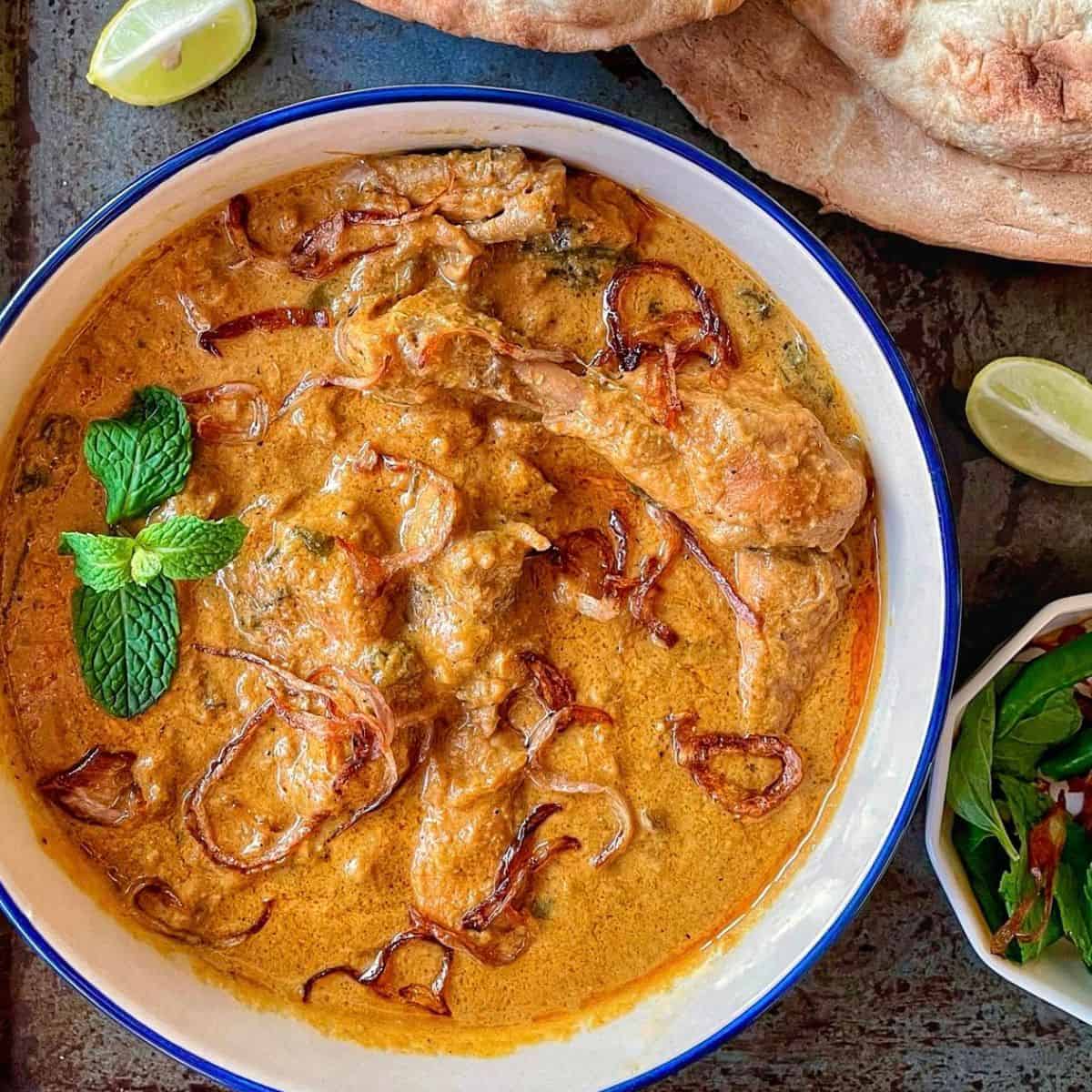 A bowl of chicken hyderabadi curry with lime wedges and naan bread.