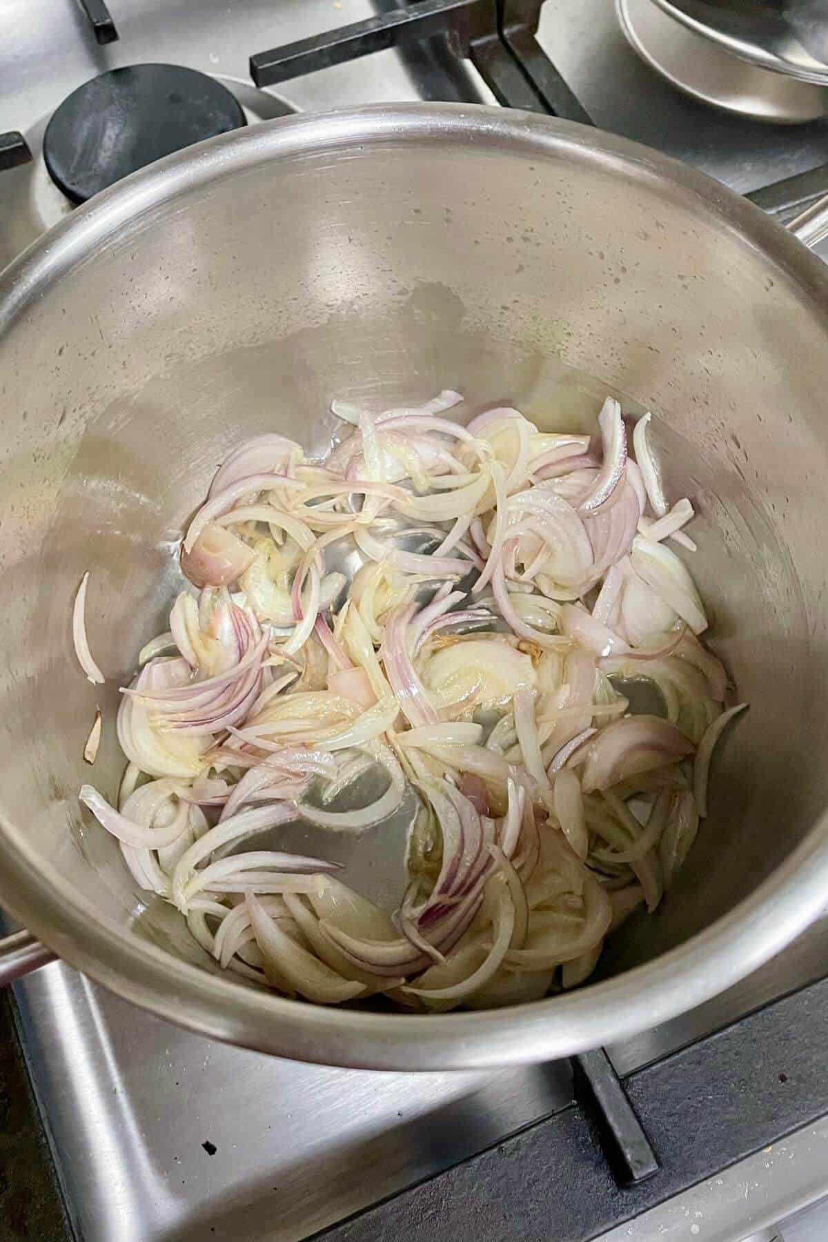 Sliced onions being sauted in a steel sauce pot. 