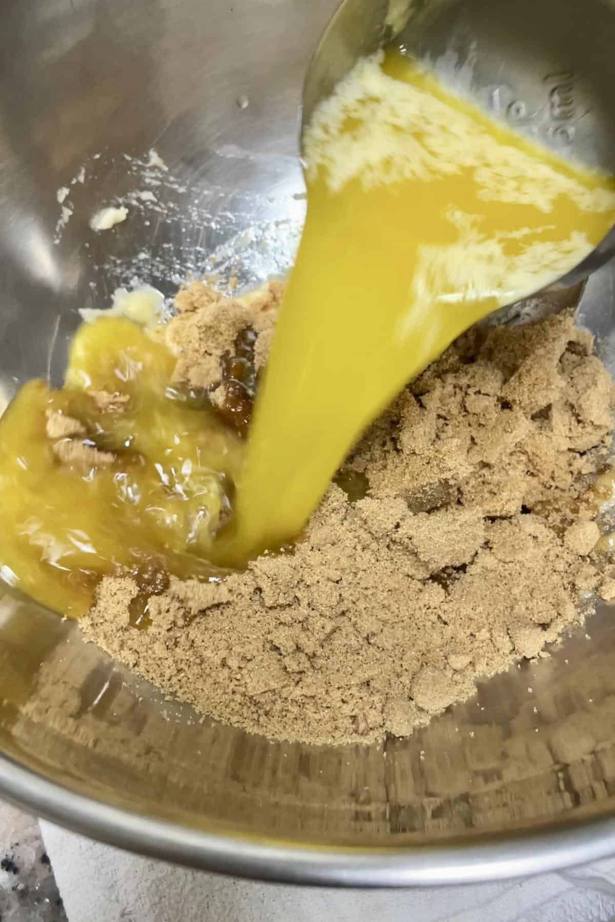 Pouring melted butter into brown sugar and mashed banana bowl.