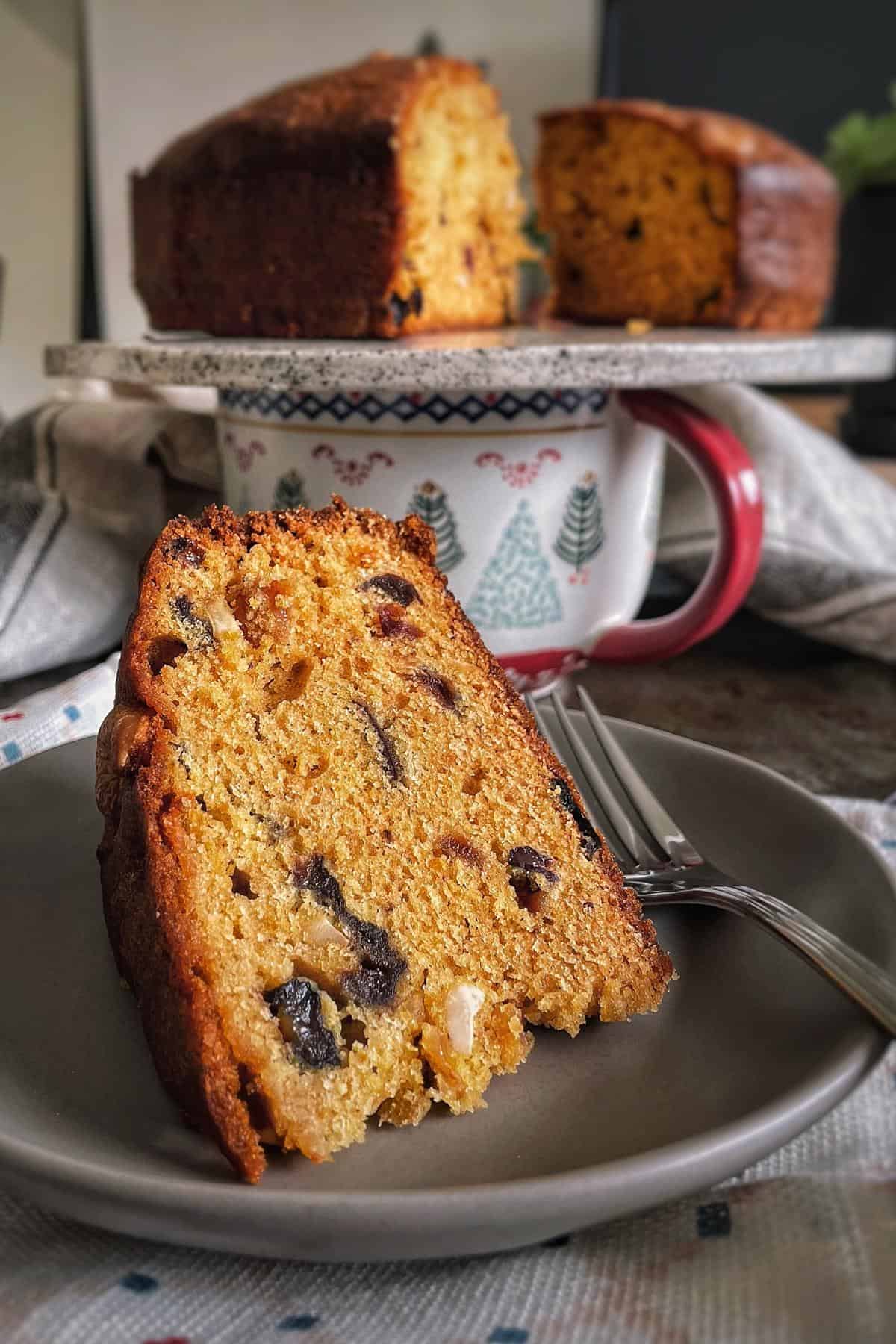 A cake stand with cut cake and a plate with sliced plum cake wedge.