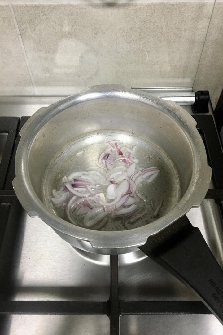 Frying sliced onions in oil in a cooker pan.