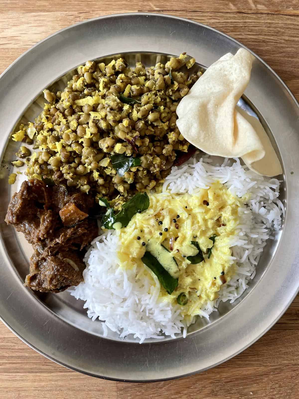 A plate of rice with moru curry poured over it. beef fry, cherupayar thora and pappad on the sides.
