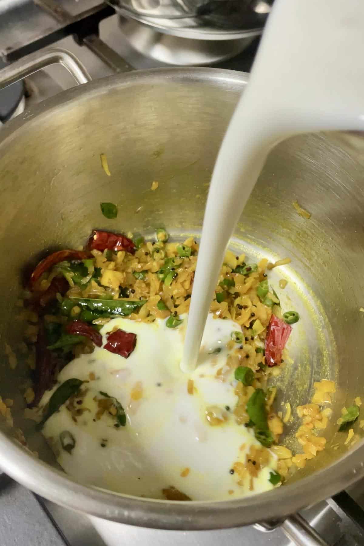 Pouring sour yoghurt water into the pot of sauted tempering of aromatics. 