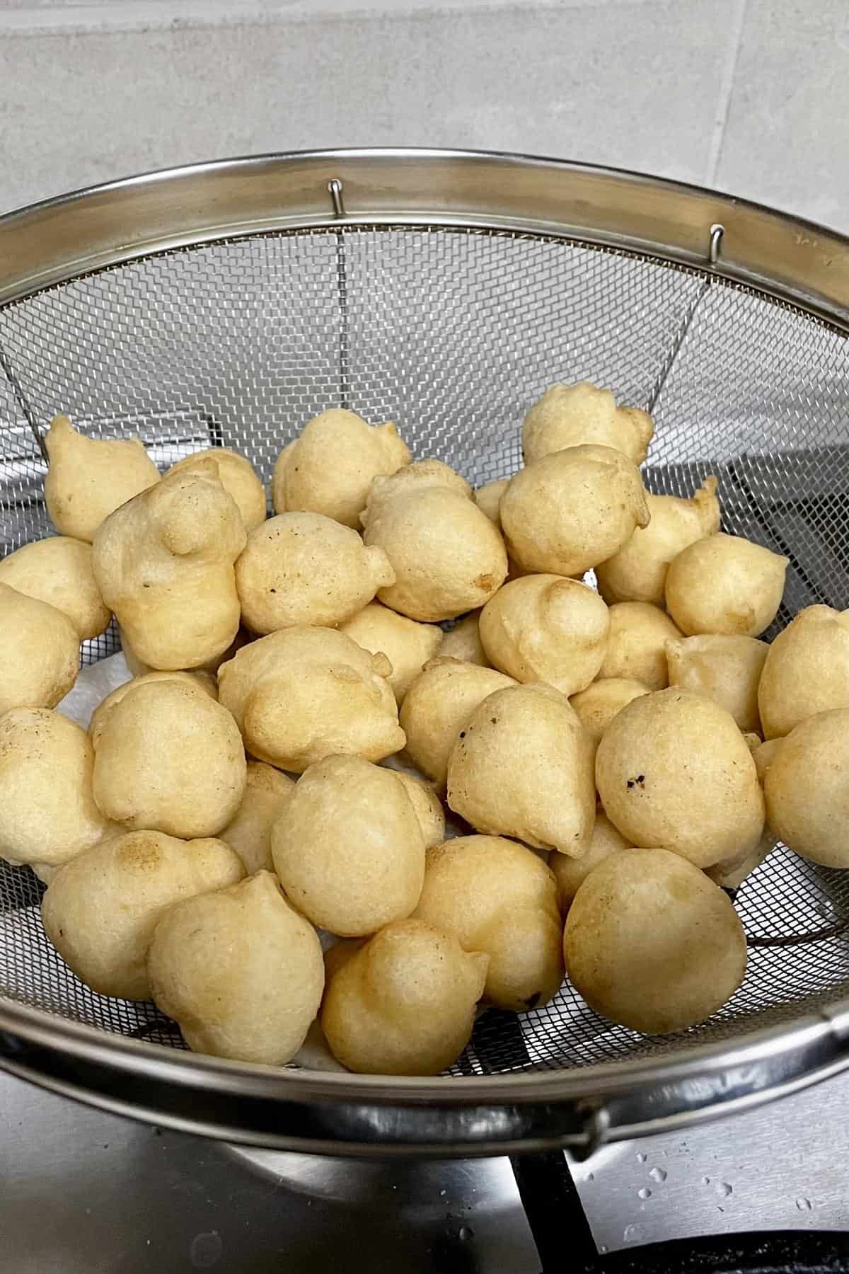 A wire colander filled with freshly fried urad dal lentil fritters.