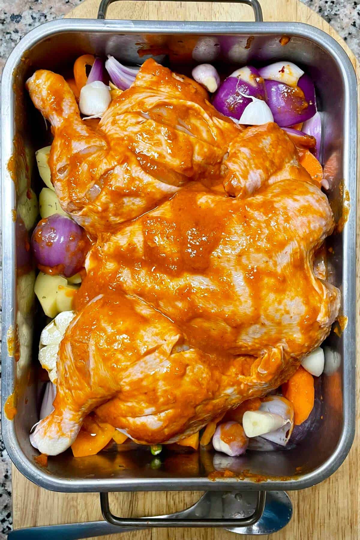 Marinated harissa chicken over bed of veggies in a roasting tin.