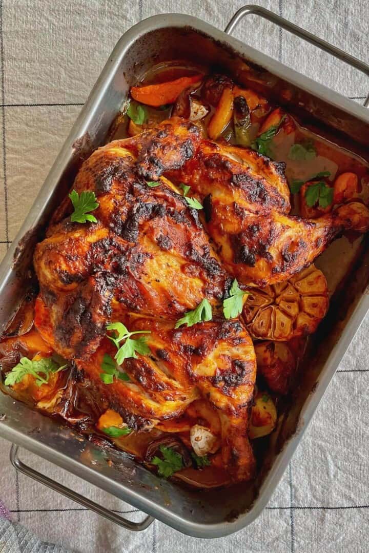 Spatchcocked chicken roast in a roasting tin with veggies and halved garlic.