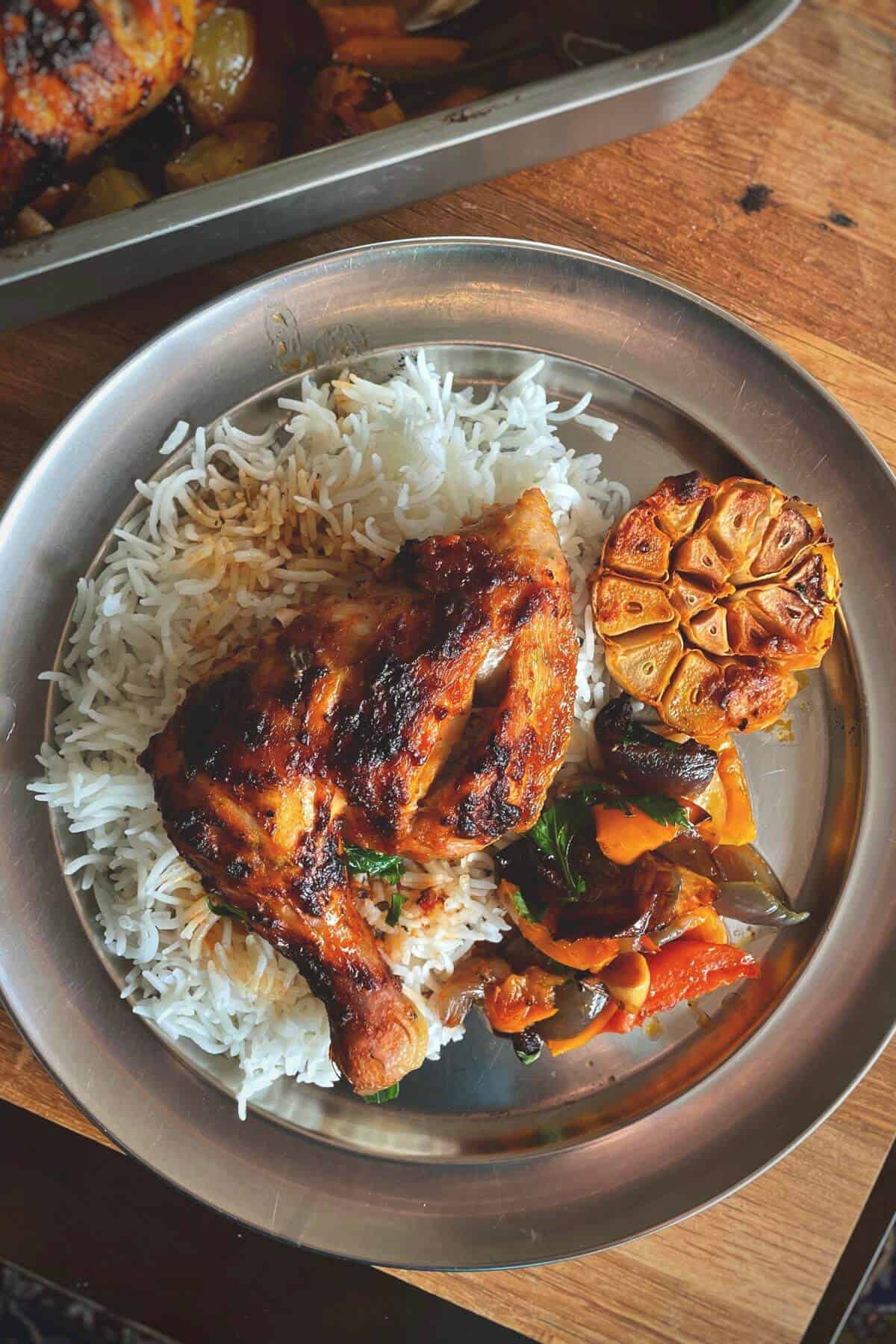 Harissa chicken leg quarter served with white rice and veggies from roasting tin.