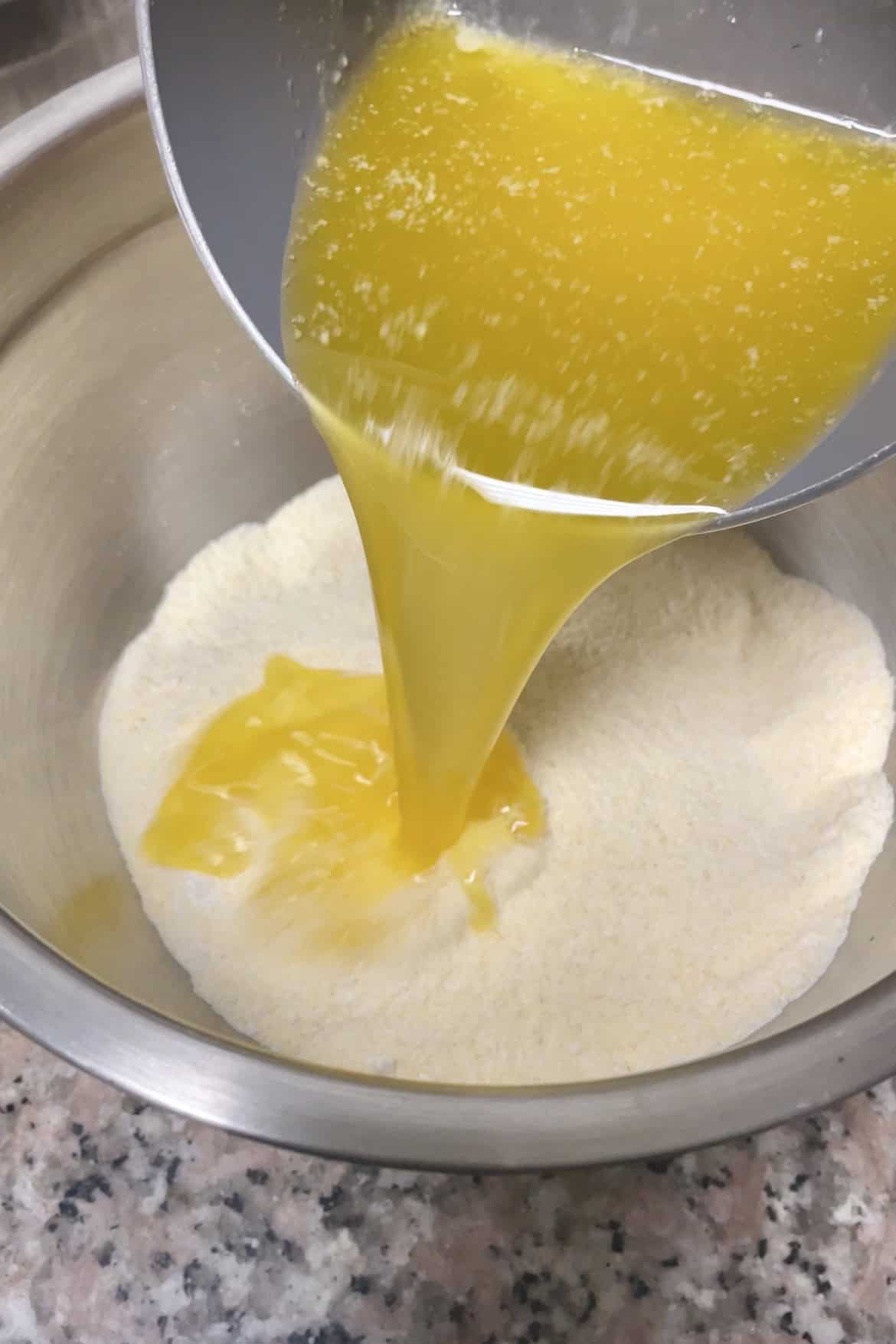 Melted ghee and butter being poured over bowl of semolina mix.