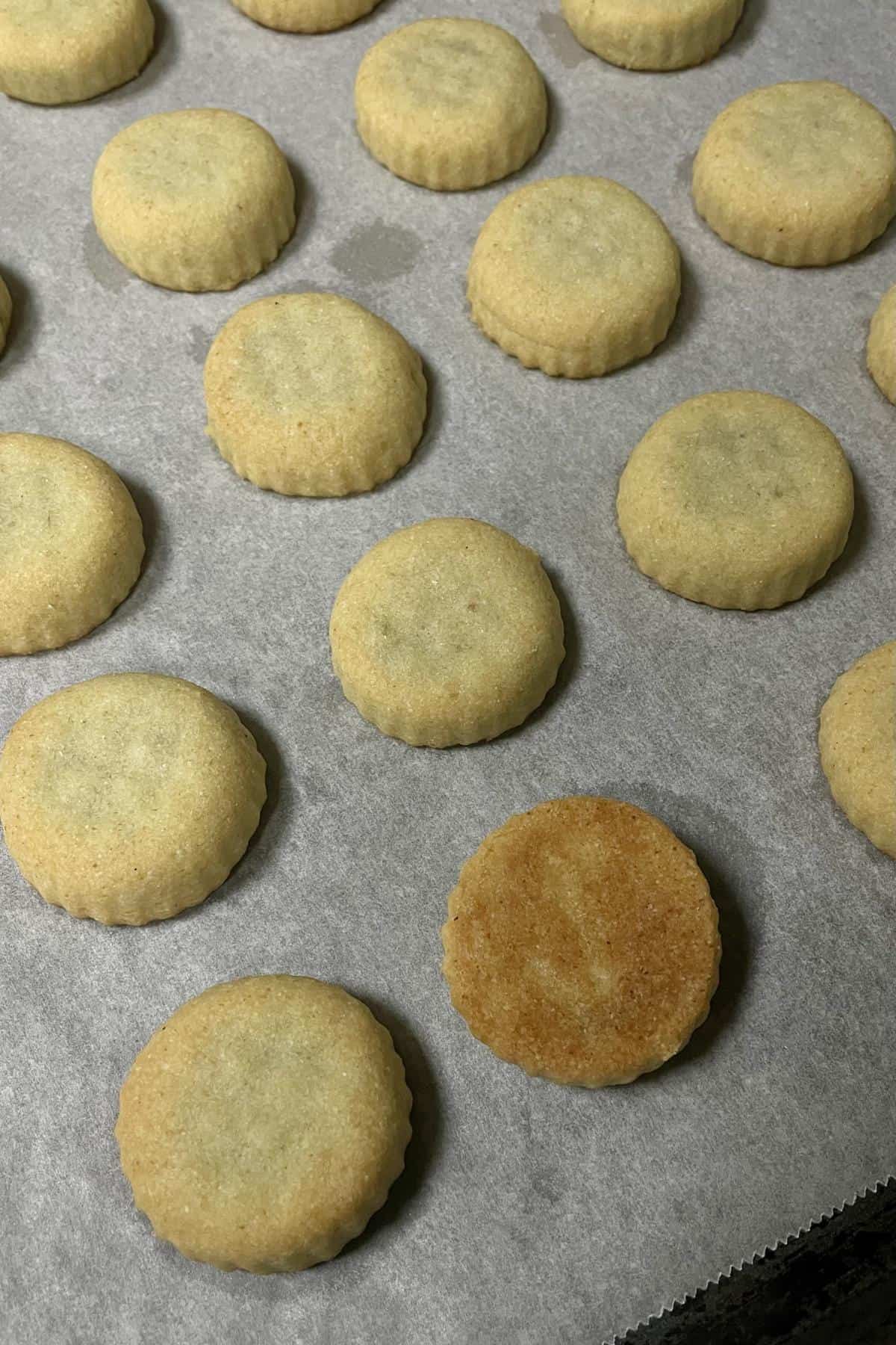 A baking tray with perfectly baked maamoul date cookies with one turned cookie.